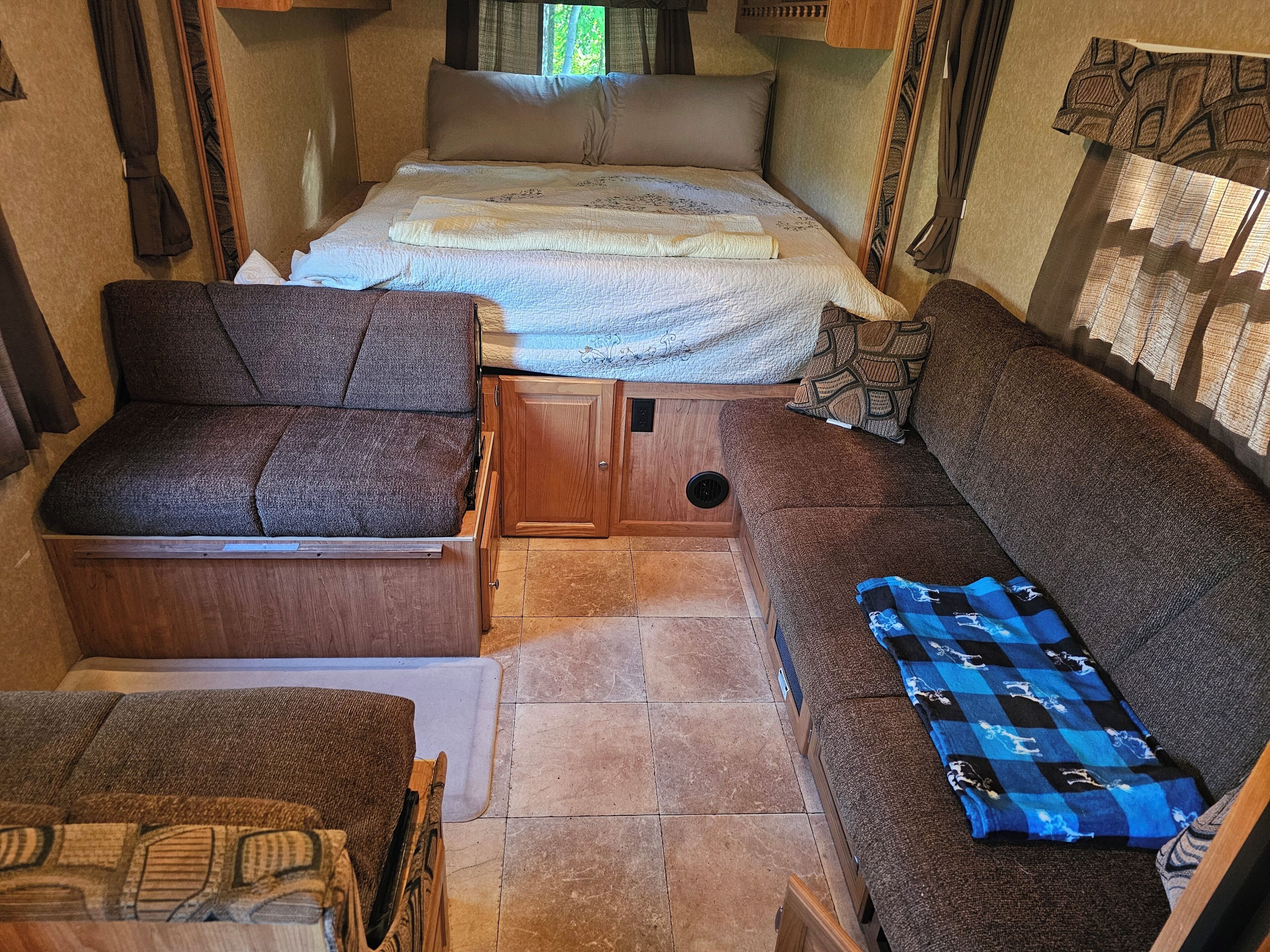 A compact RV interior with a bed, a sofa, a chair, and a small table.. Cozy Camper on Expansive Vermont Property