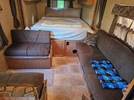 A compact RV interior with a bed, a sofa, a chair, and a small table.. Cozy Camper on Expansive Vermont Property