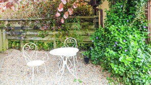 Ein Garten mit zwei weißen Metallstühlen und einem Tisch, umgeben von Kies und einem Holzzaun.