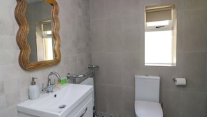 Ein Badezimmer mit weißem Waschbecken, Toilette, Spiegel mit Holzrahmen und Fenster mit Jalousien.