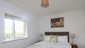 Ein Schlafzimmer mit Bett, Fenster, Heizkörper, Gemälde und Nachttisch mit Lampe.