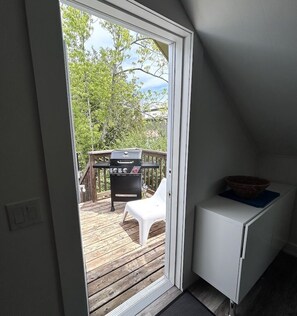 A room with a sliding door leading to an outdoor deck with a grill and a white chair.