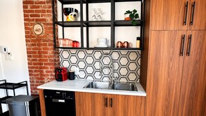 A compact kitchen with a dishwasher, a sink, a black cabinet, a wooden cabinet, and a brick wall. - Historic Bruce House | Hot Tub, Fire Pit &AC (Shelburne)