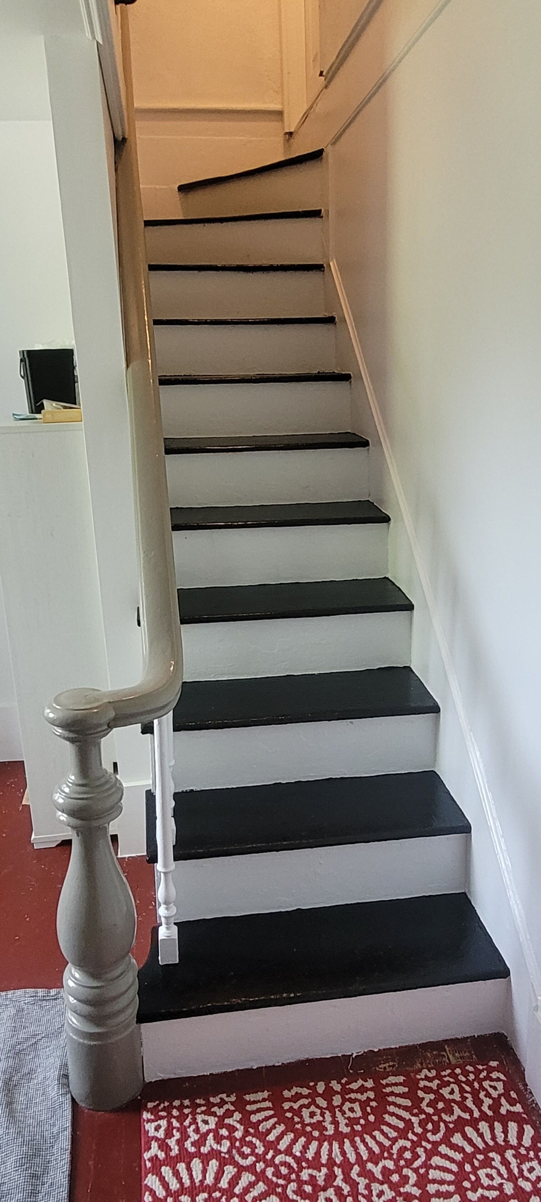 Een trap met zwarte treden en witte wanden, die uitkomt op een plateau met een witte deur.