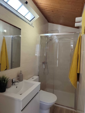 Et moderne badeværelse med en glasbrusekabine, en hvid vask og et toilet.