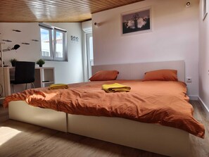 Ein Schlafzimmer mit Bett, Kissen, Schreibtisch, Stuhl, Fenster und Wanddekorationen.