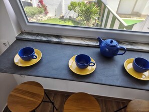 Ein Fensterplatz mit vier blauen Tassen und Untertassen, einer blauen Teekanne und Blick auf einen Garten.