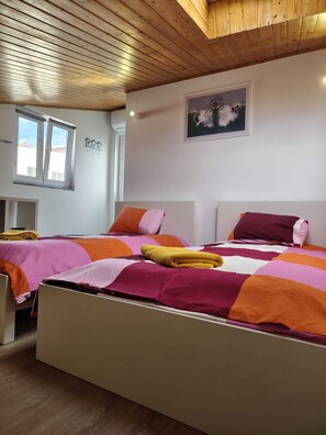 Ein Schlafzimmer mit zwei Betten, Holzboden, einem Fenster, einem Wandbild und einem kleinen Regal.
