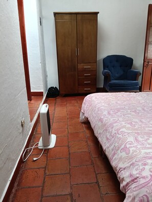 Ein Schlafzimmer mit Bett, Kleiderschrank, Stuhl und Heizlüfter.
