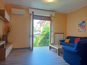 Ein Wohnzimmer mit einem blauen Sofa, einem kleinen Couchtisch und Blick auf einen Balkon mit grüner Brüstung.