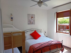 A bedroom with a bunk bed, a single bed with a red pillow, a ceiling fan, a window with blinds, and a painting on the wall. - Detached house, A/C, free parking, big garden, patio and Solarium with shower (Como)