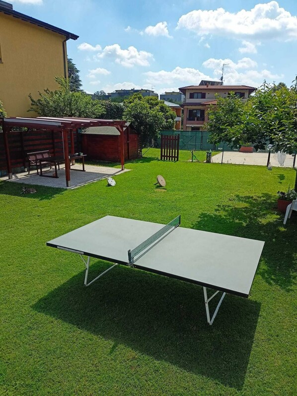 A ping pong table in a grassy outdoor area with a wooden bench and a small shed in the background. - Detached house, A/C, free parking, big garden, patio and Solarium with shower (Como)