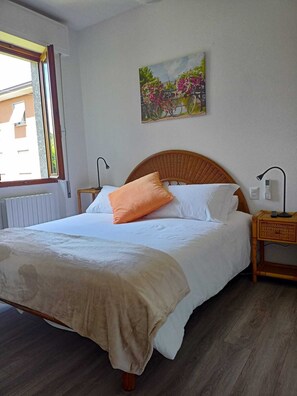 Ein Schlafzimmer mit Bett, Nachttisch, Lampe, Gemälde und Fenster.