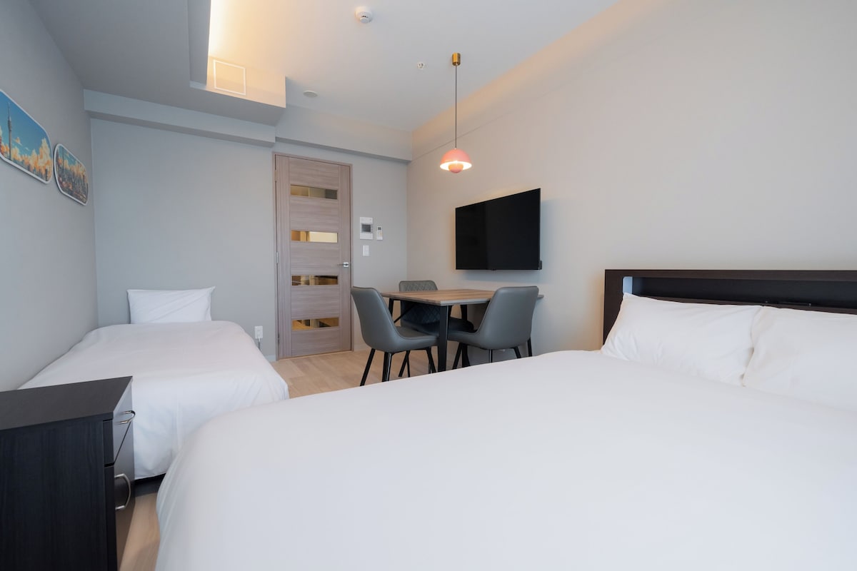 Ein Hotelzimmer mit zwei Betten, einem Schreibtisch mit Stühlen, einem Fernseher und einer Tür mit Fenster.