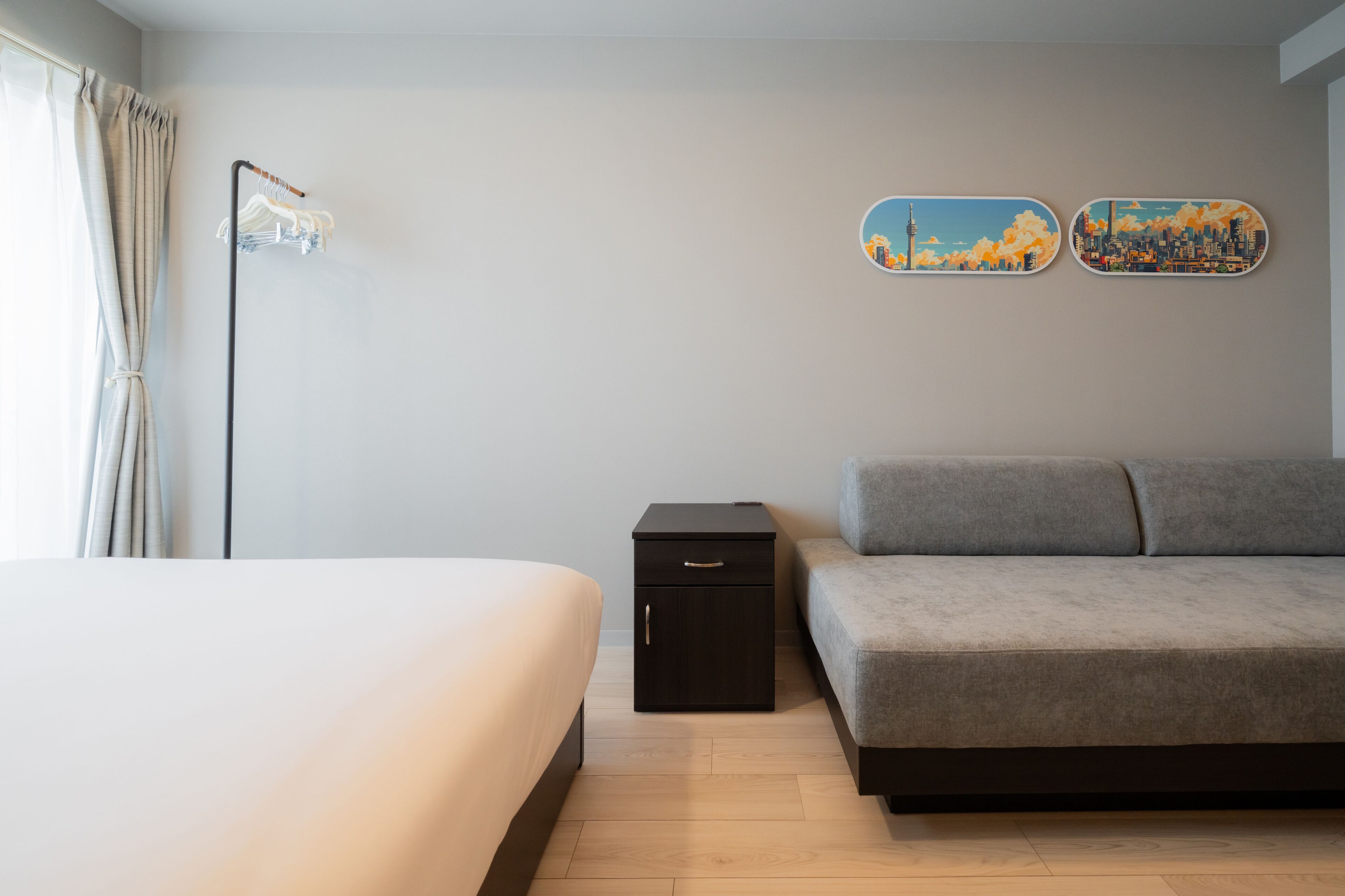 Une chambre à coucher avec un lit, une petite table de chevet, un canapé gris et deux œuvres d’art murales.