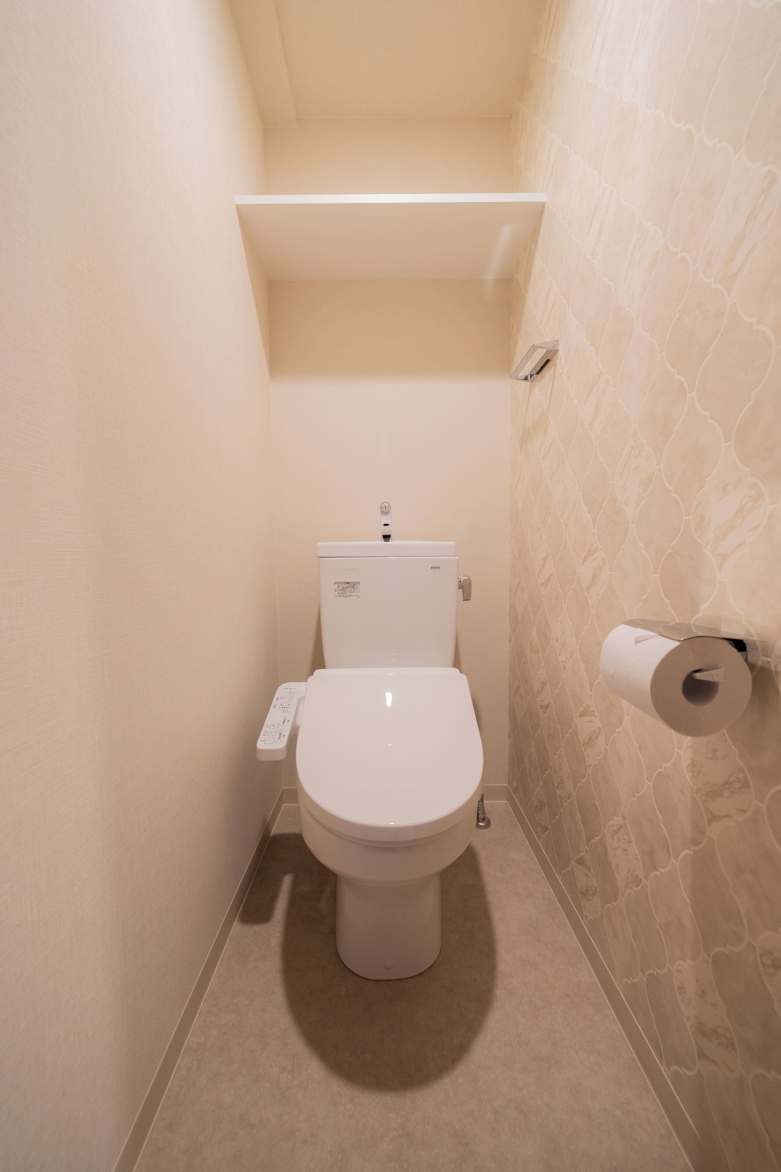 A small, narrow bathroom with a toilet, a paper towel dispenser, and a wall-mounted toilet paper holder.