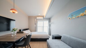 Ett modernt hotellrum med en säng, en soffa, ett matbord med stolar, en TV och ett fönster med gardiner.