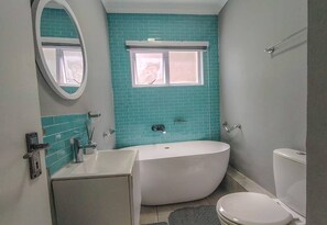 A bathroom with a bathtub, toilet, and a window. - Coastal Chic in the Heart of Ballito 3-bed Oasis (Ballito)