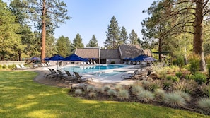 A pool area with lounge chairs and umbrellas, surrounded by trees and a building with a stone facade. - New! Affordable Mountain Escape | Pool - Hot Tub | Near Mt. Bachelor (Bend)