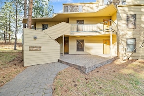 A two-story building with a wooden exterior, a covered entrance, and a small outdoor area with a brick pathway. - New! Affordable Mountain Escape | Pool - Hot Tub | Near Mt. Bachelor (Bend)