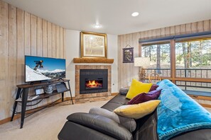 A living room with a fireplace, a television, and a sofa with colorful cushions. - New! Affordable Mountain Escape | Pool - Hot Tub | Near Mt. Bachelor (Bend)