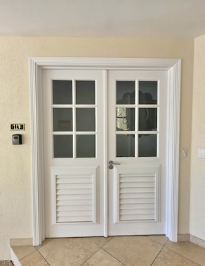 A double door with frosted glass panels, a doorbell, and a light switch on the wall. - Sapphire 117 - 2 Bedroom Condo at Sapphire Beach on Dover Beach Barbados (Bridgetown)