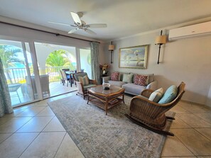 A spacious living area with a sliding glass door leading to a balcony, a ceiling fan, a sofa with patterned cushions, and a dining table with chairs. - Sapphire 117 - 2 Bedroom Condo at Sapphire Beach on Dover Beach Barbados (Bridgetown)