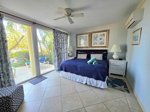 Quarto com cama, ventoinha no teto, mesa de cabeceira, abajur e janela com cortinas.