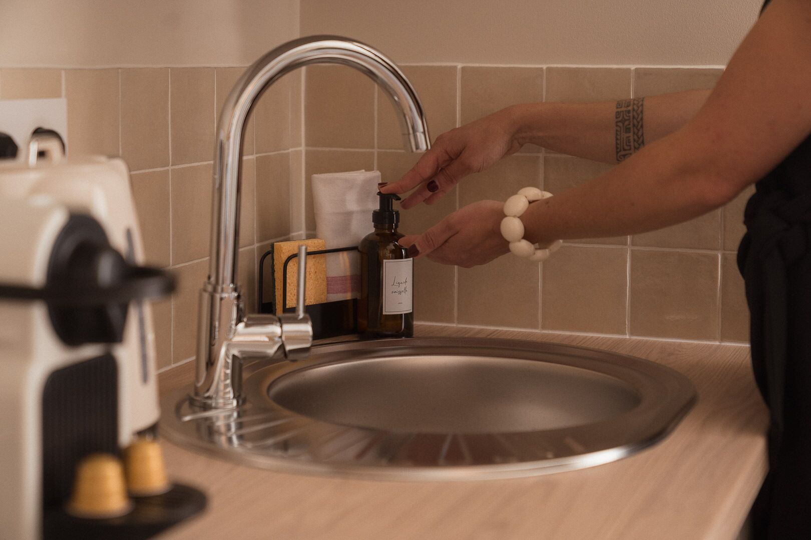 A person using a kitchen sink with a faucet, soap dispenser, and sponge rack.