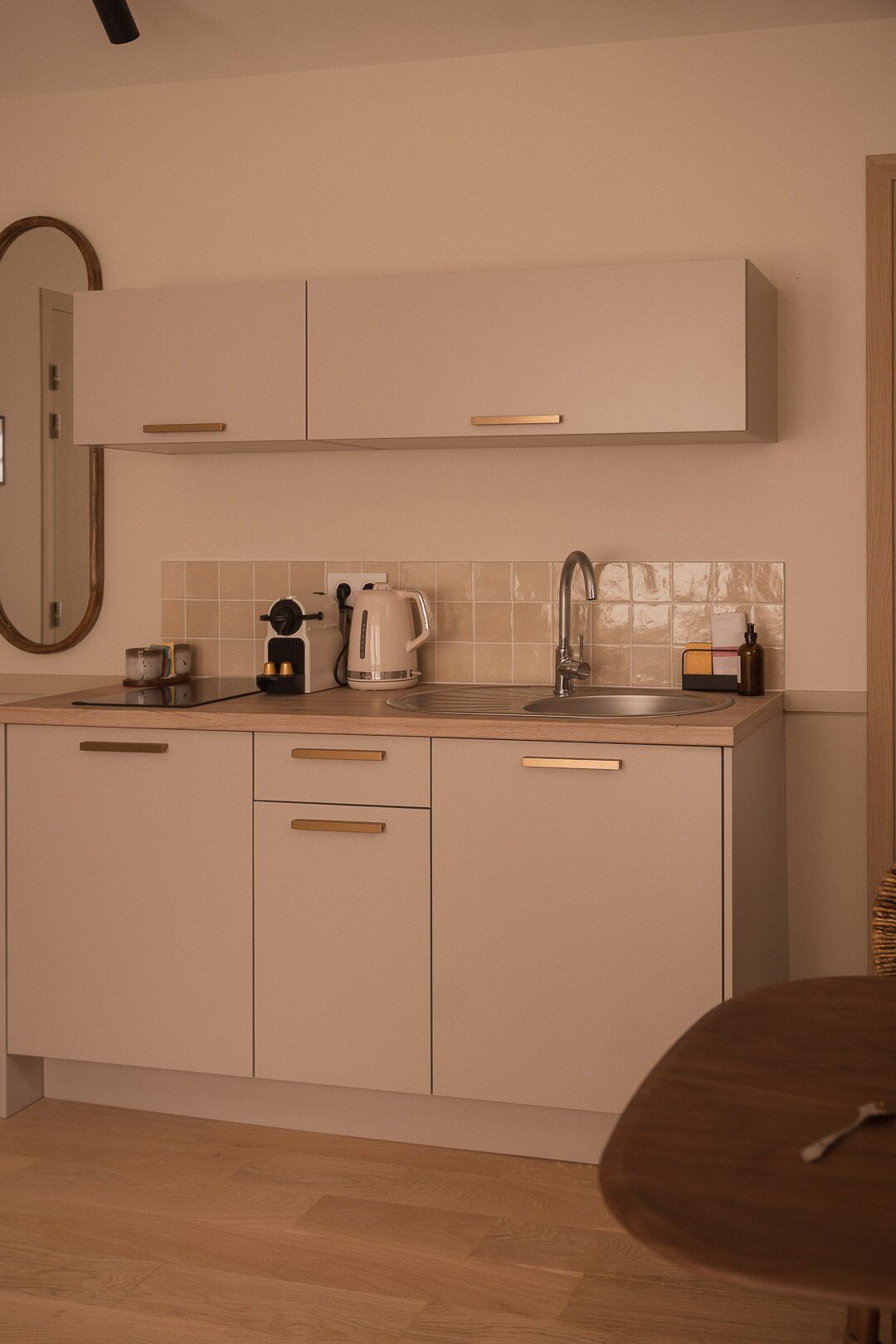 A modern kitchen with light-colored cabinets, a stainless steel sink, and a wooden dining table.