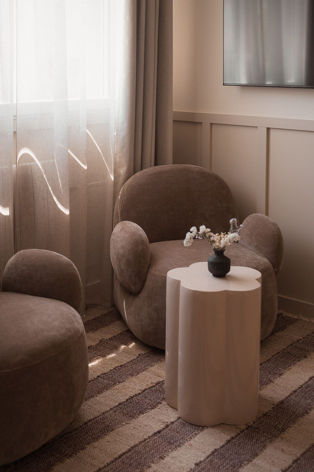 A room with a sofa, a round side table, and a vase with flowers.