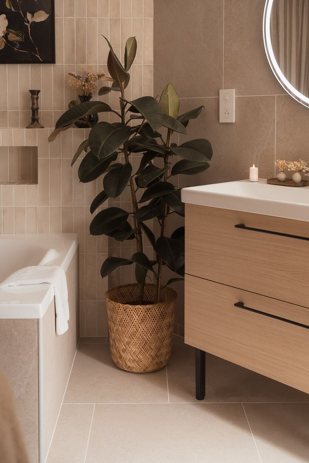 Un baño con un mueble de madera, una planta en una cesta tejida, una bañera blanca y un espejo montado en la pared.