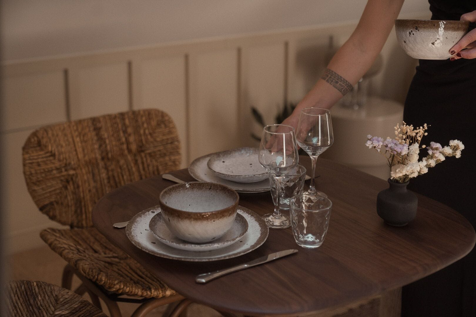 A dining table set with plates, glasses, and a vase with flowers.