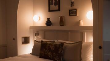 A bedroom with a bed, pillows, a nightstand, a wall-mounted shelf with decorative items, and wall sconces.
