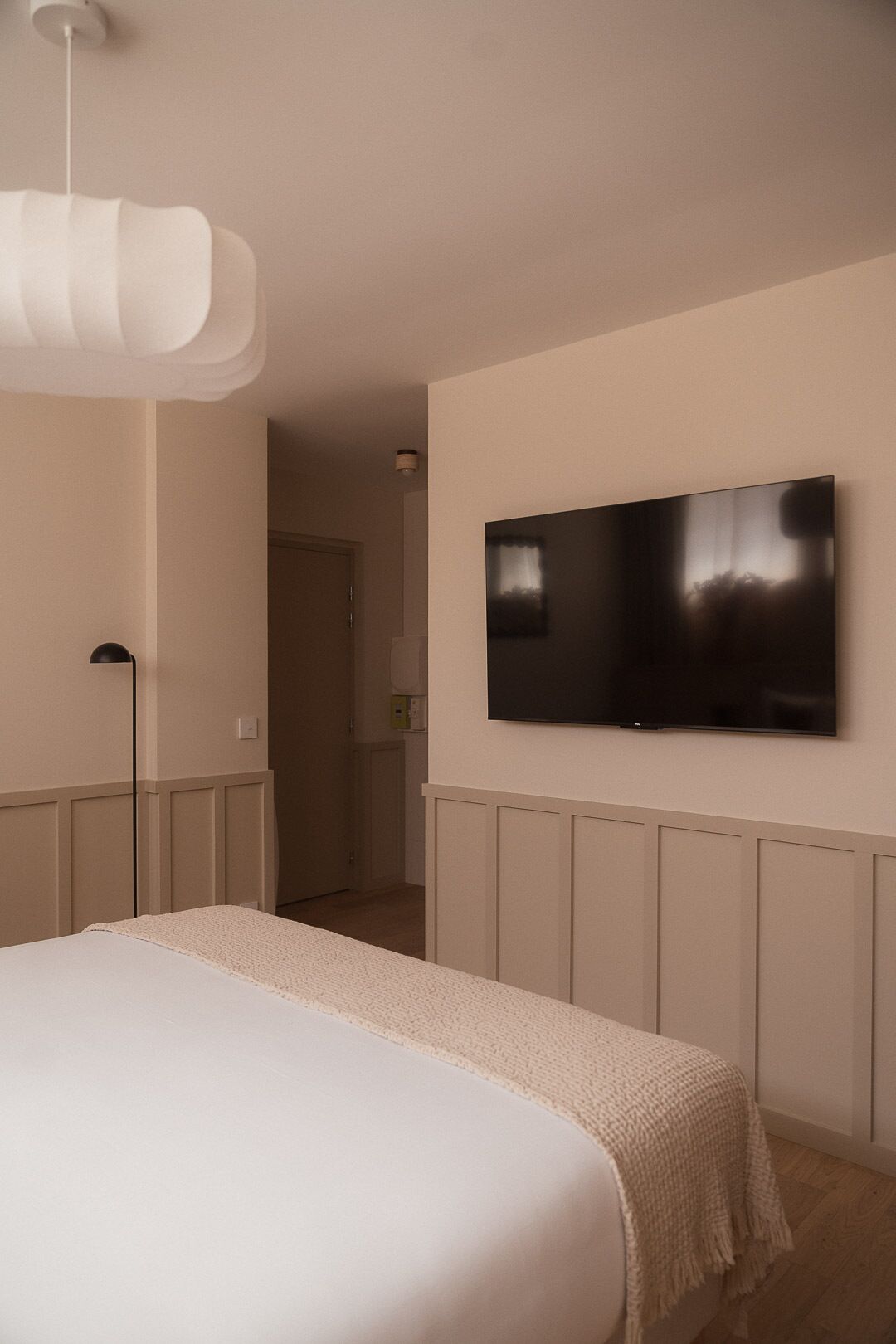 Une chambre à coucher avec un lit, un téléviseur fixé au mur et un luminaire suspendu.