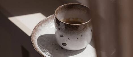 A cup on a saucer by a window with a curtain partially drawn.