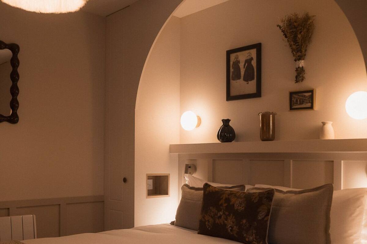 A bedroom with a large bed, an arched ceiling, a bedside table, and wall-mounted lighting.