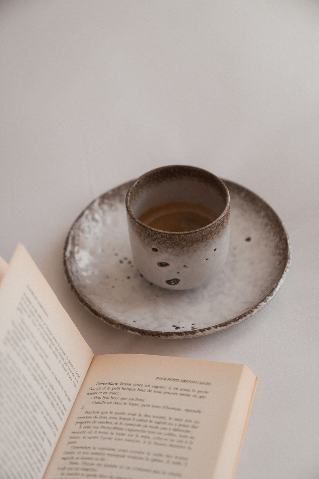 Een kop koffie op een schotel naast een open boek.