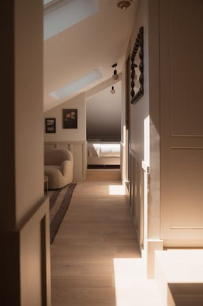 Un pasillo estrecho con techo inclinado, una cama a lo lejos y una silla en primer plano.