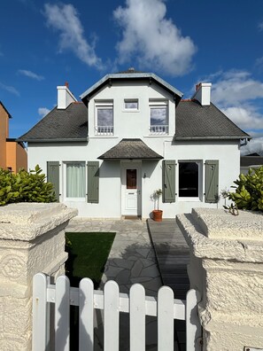 Ein zweigeschossiges Haus mit weißer Fassade, einer Veranda und einem weißen Zaun.