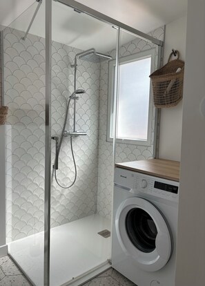 Ein kleines Badezimmer mit Dusche, Waschmaschine und Fenster.