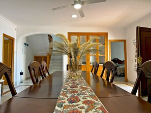 Ein Esszimmer mit einem langen Tisch, Stühlen, einem Deckenventilator und einer Zierpflanze.