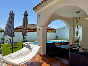 Ein überdachter Außenbereich mit einer Hängematte, Terrassenmöbeln und einem Pool.