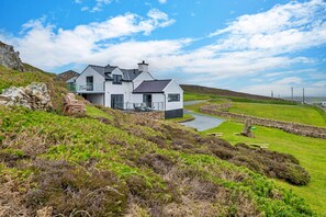 A modern house with a stone staircase, a pond, and a grassy landscape. - Goferydd (Holyhead)