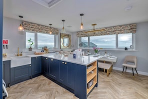 A modern kitchen with a large island, dark blue cabinets, and a herringbone floor pattern. - Goferydd (Holyhead)