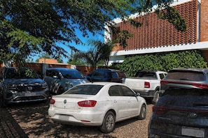Un parking où sont garées plusieurs voitures, dont une Volkswagen blanche et une Kia noire, devant un bâtiment à la façade en briques et orné de verdure.