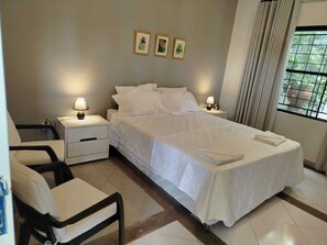 Une chambre d’hôtel avec un lit, deux tables de chevet avec des lampes, une chaise et une fenêtre avec des rideaux.
