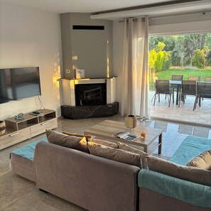 Ein modernes Wohnzimmer mit Flachbildfernseher, Kamin, einer Couch und einem Essbereich mit Stühlen.