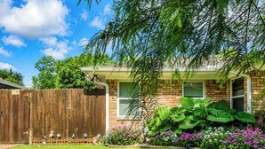 A house with a brick exterior, a wooden fence, and a well-maintained garden with various plants and flowers. - FIFA26 Chic Suite - Near NRG  (Houston)