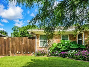 Ein Haus mit Ziegelaußenwand, Holzzaun und einem gepflegten Garten mit verschiedenen Pflanzen und Blumen.